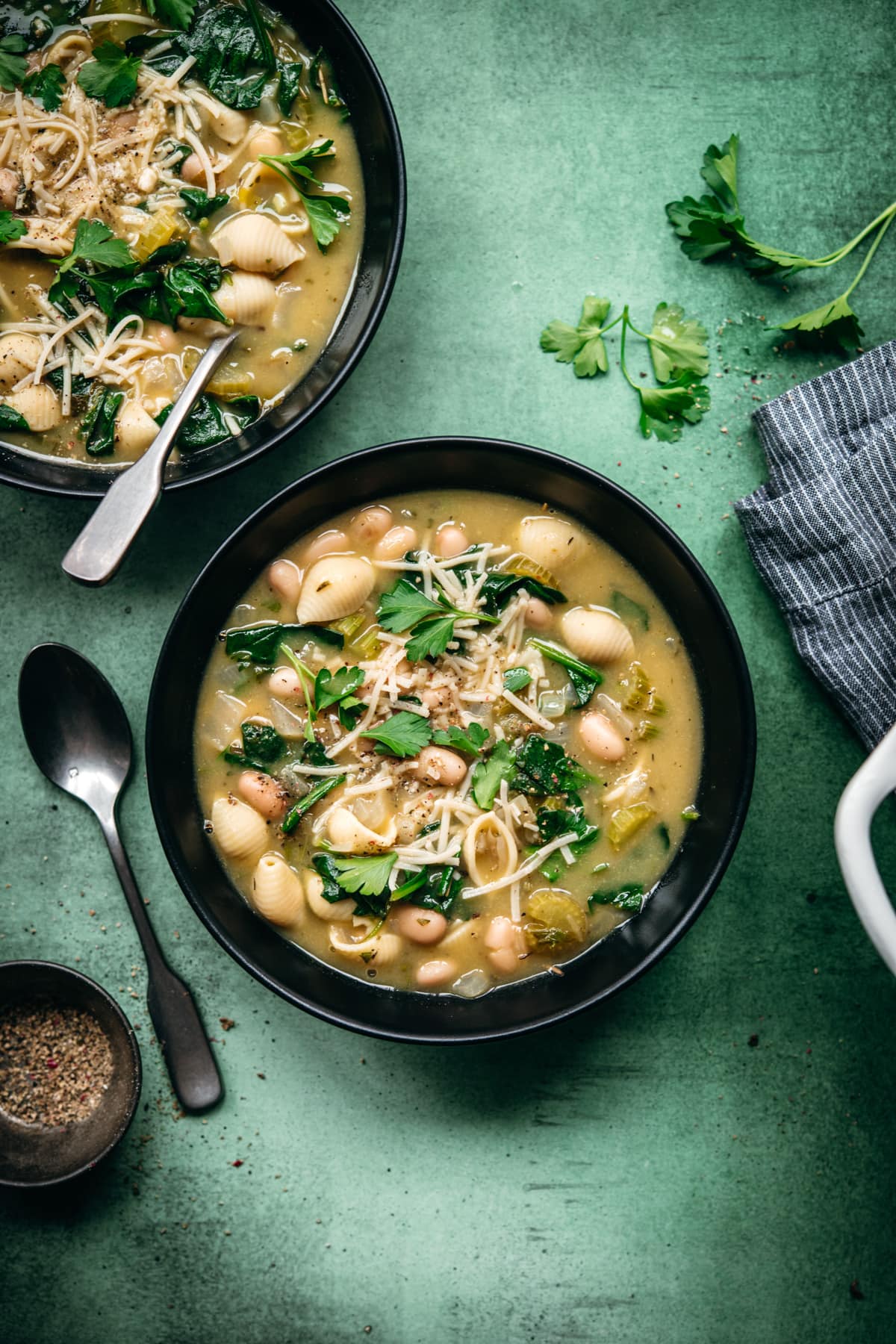 overhead view of white bean spinach soup topped with vegan parmesan in black soup bowl. 