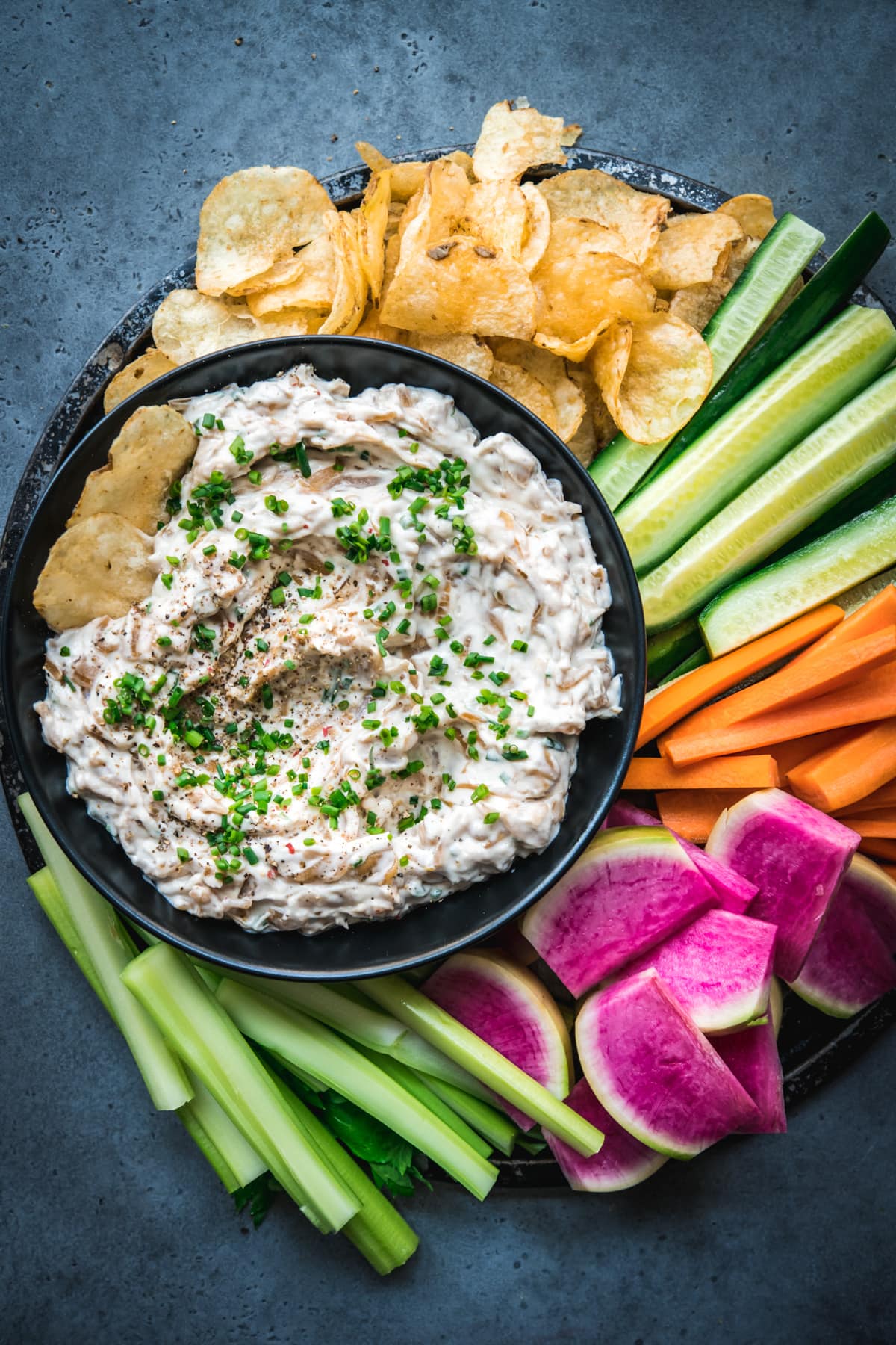 overhead view of vegan caramelized onion dip on a platter with chips and vegetables. 