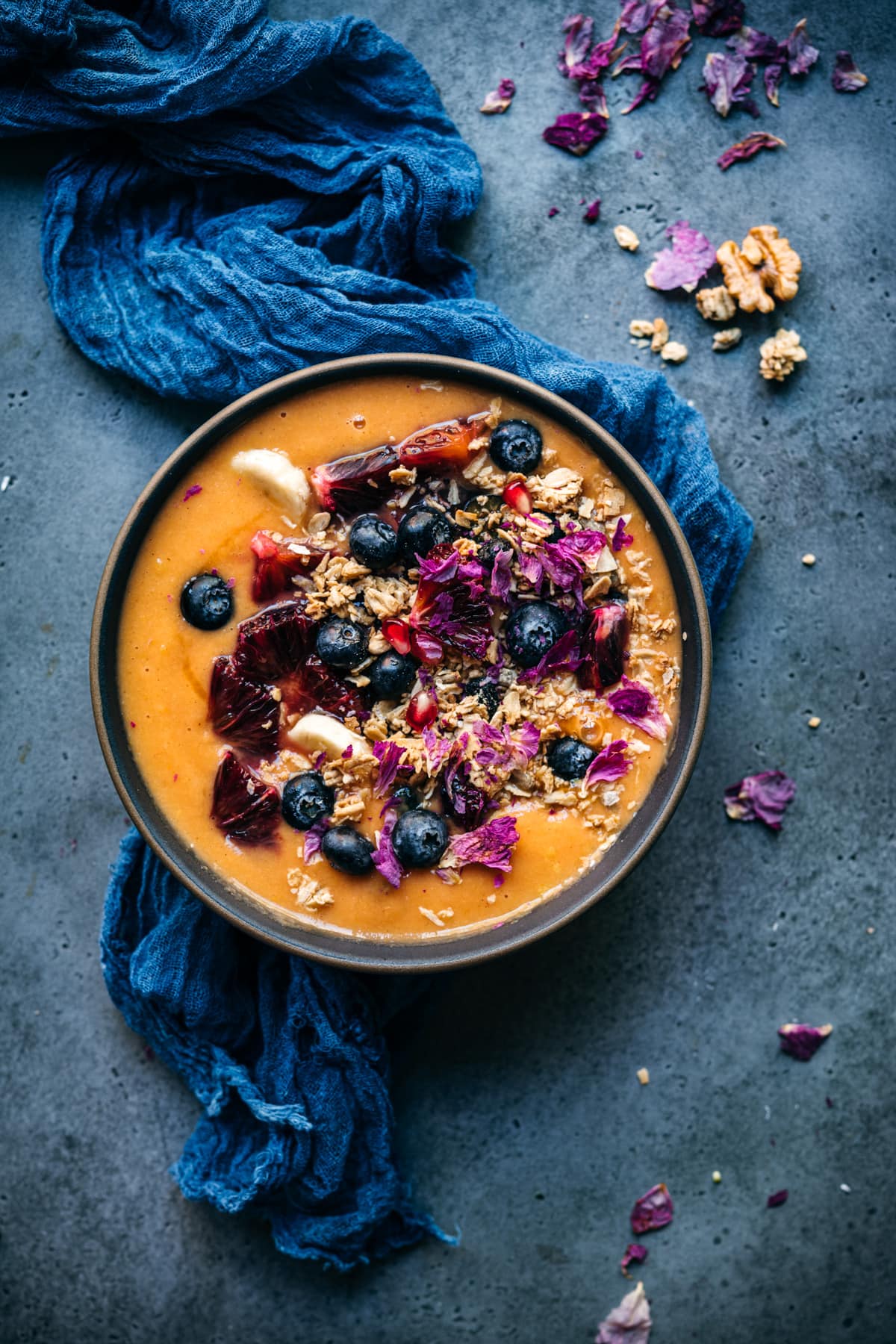 overhead view of citrus carrot smoothie bowl topped with fresh fruit and granola. 