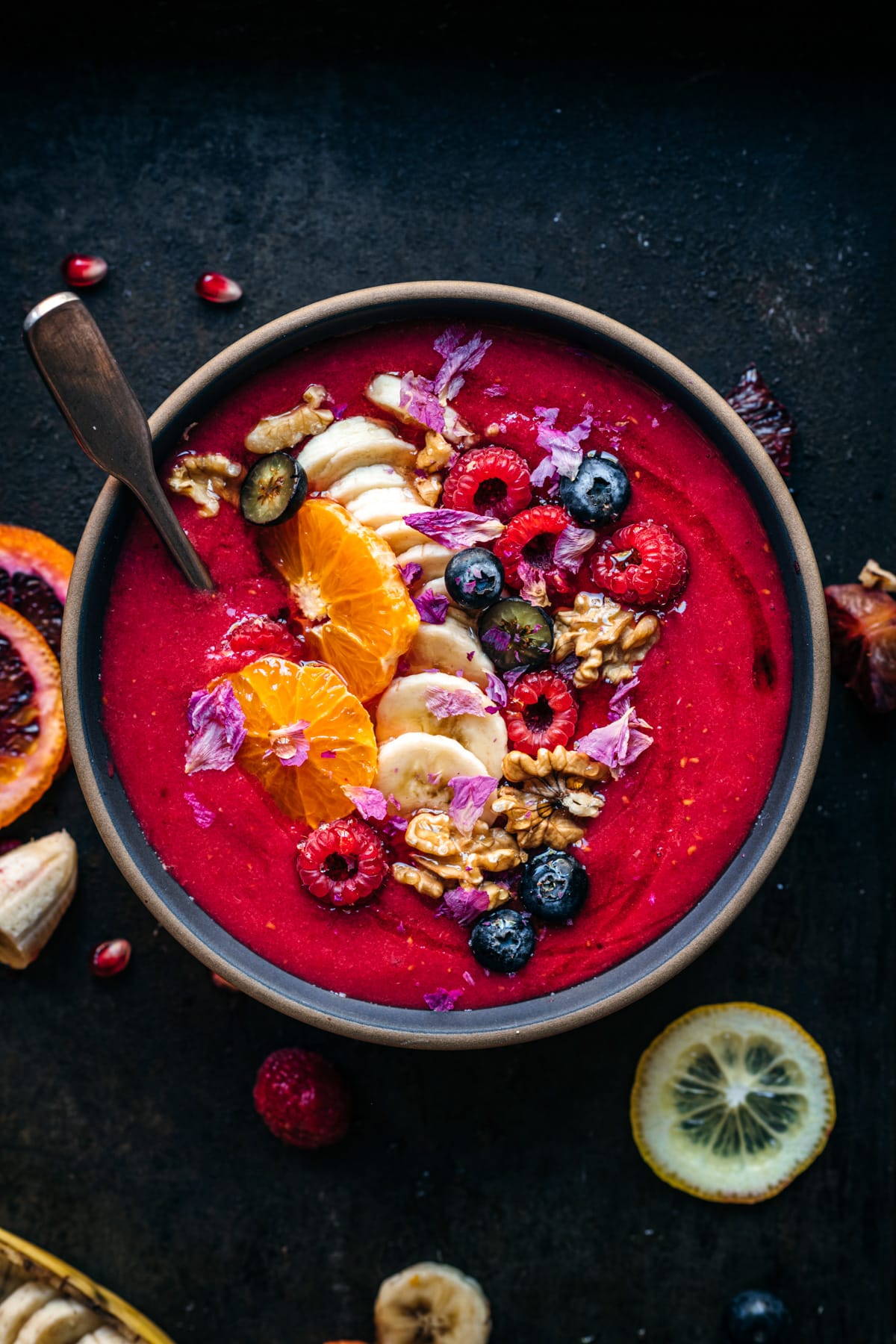 overhead view of multiple red, orange and yellow smoothie bowls with fresh fruit and granola toppings.