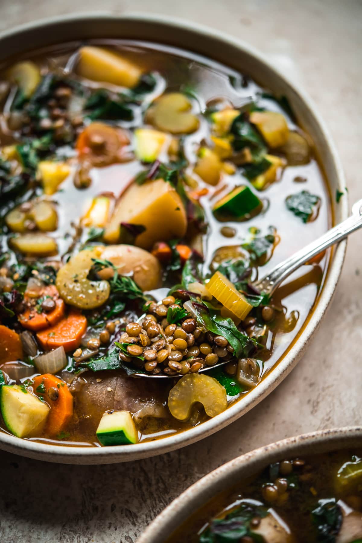 close up view of lentil soup on a spoon in a bowl.