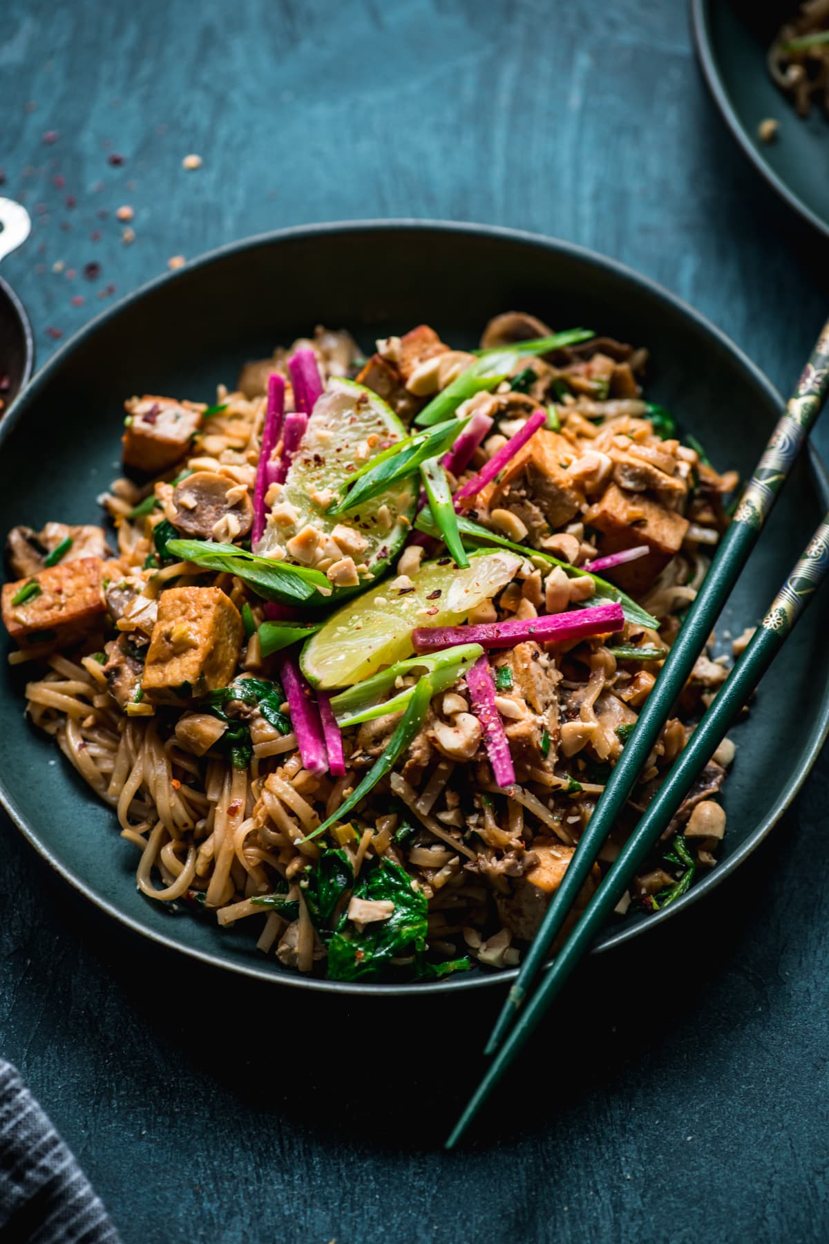 close up view of vegan tofu pad thai in a blue bowl topped with lime and radish. 