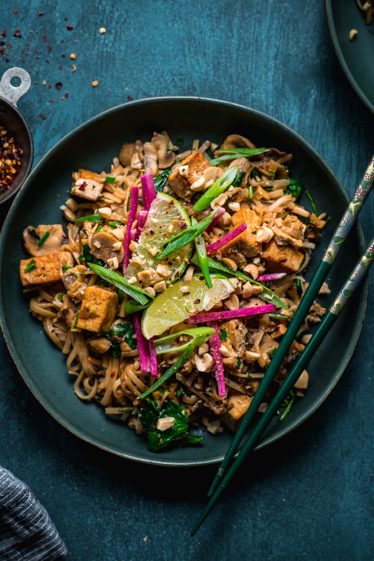 overhead view of vegan pad thai with tofu in a blue bowl with chopsticks. 