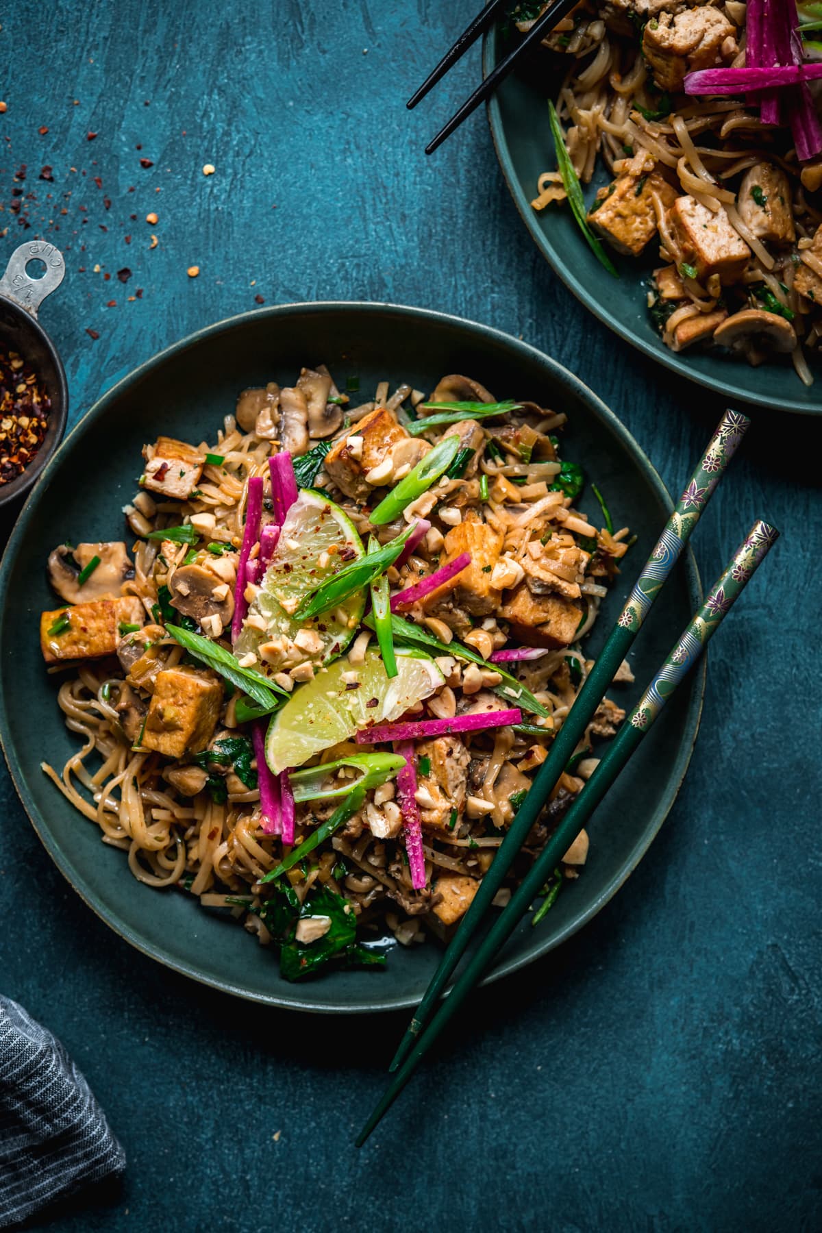 overhead view of vegan pad thai with tofu in a blue bowl with chopsticks. 