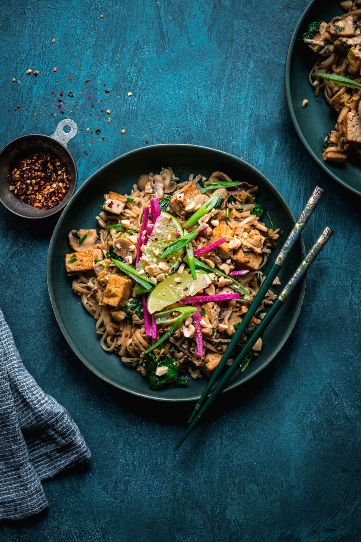 overhead view of vegan pad thai with tofu in a blue bowl with chopsticks. 