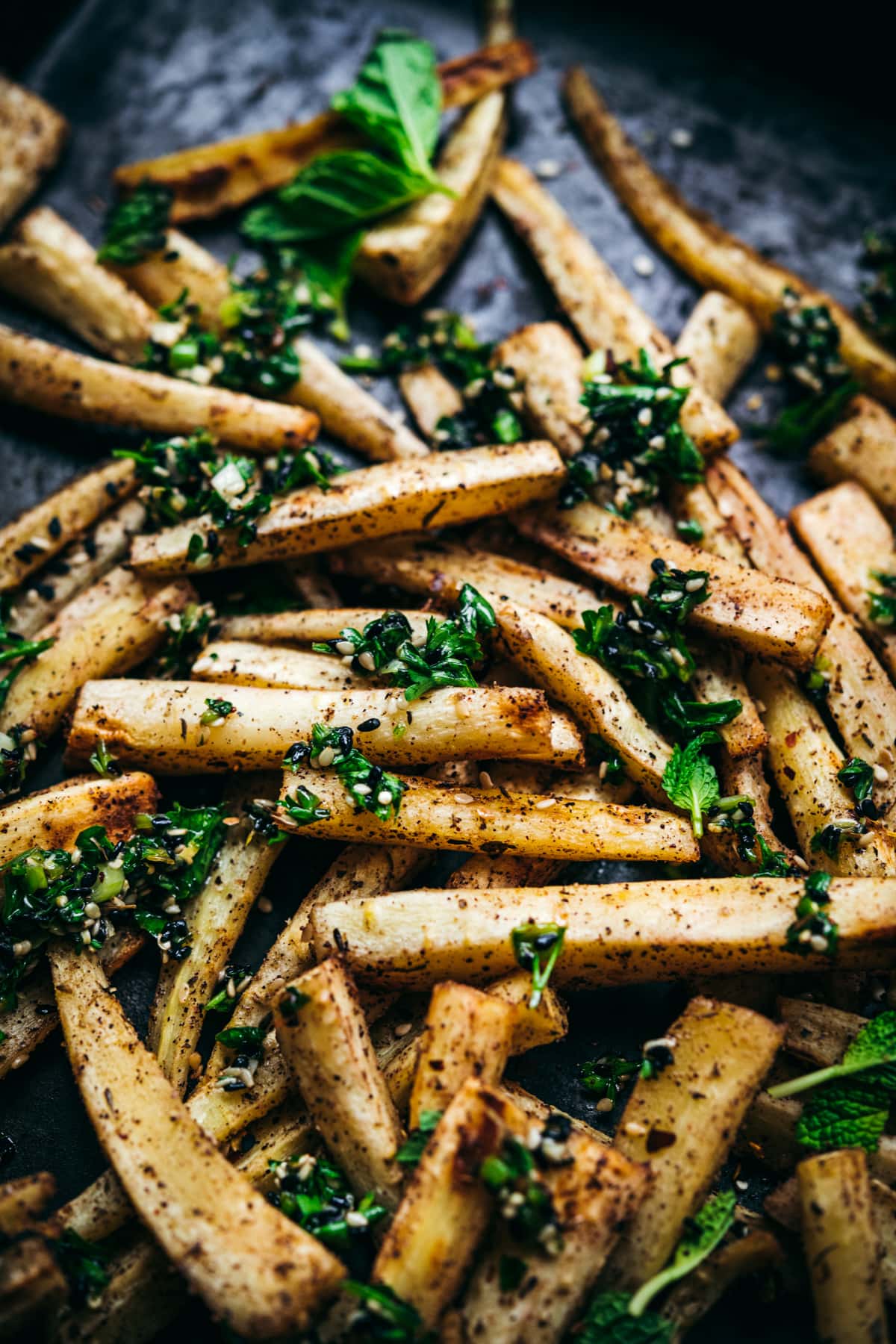 close up view of roasted parsnips on a sheet pan with za'atar gremolata on top. 