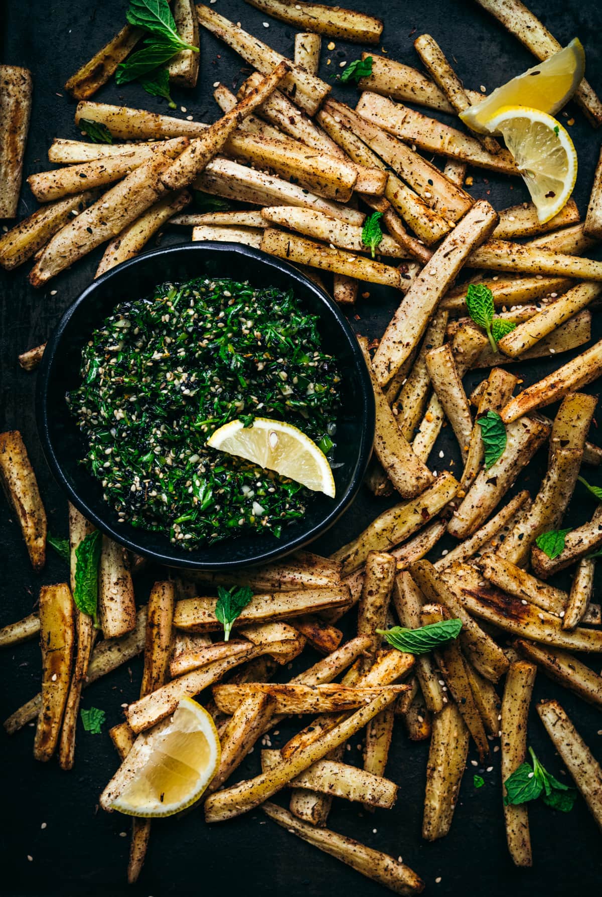 overhead view of roasted parsnips on a sheet pan with a bowl of za'atar gremolata. 