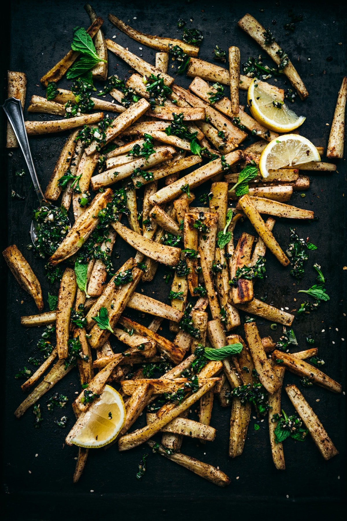 overhead view of roasted parsnips on a sheet pan with za'atar gremolata on top.
