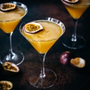 close up view of a passion fruit martini in a glass with dark backdrop.