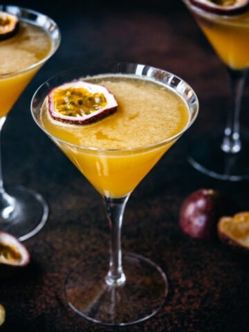 close up view of a passion fruit martini in a glass with dark backdrop.