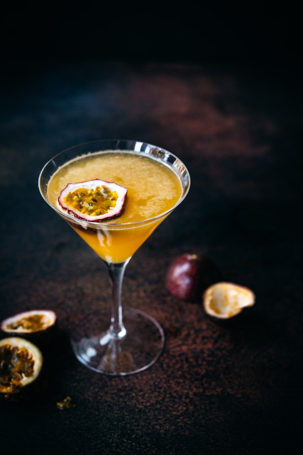 close up view of a passion fruit martini in a glass with dark backdrop. 