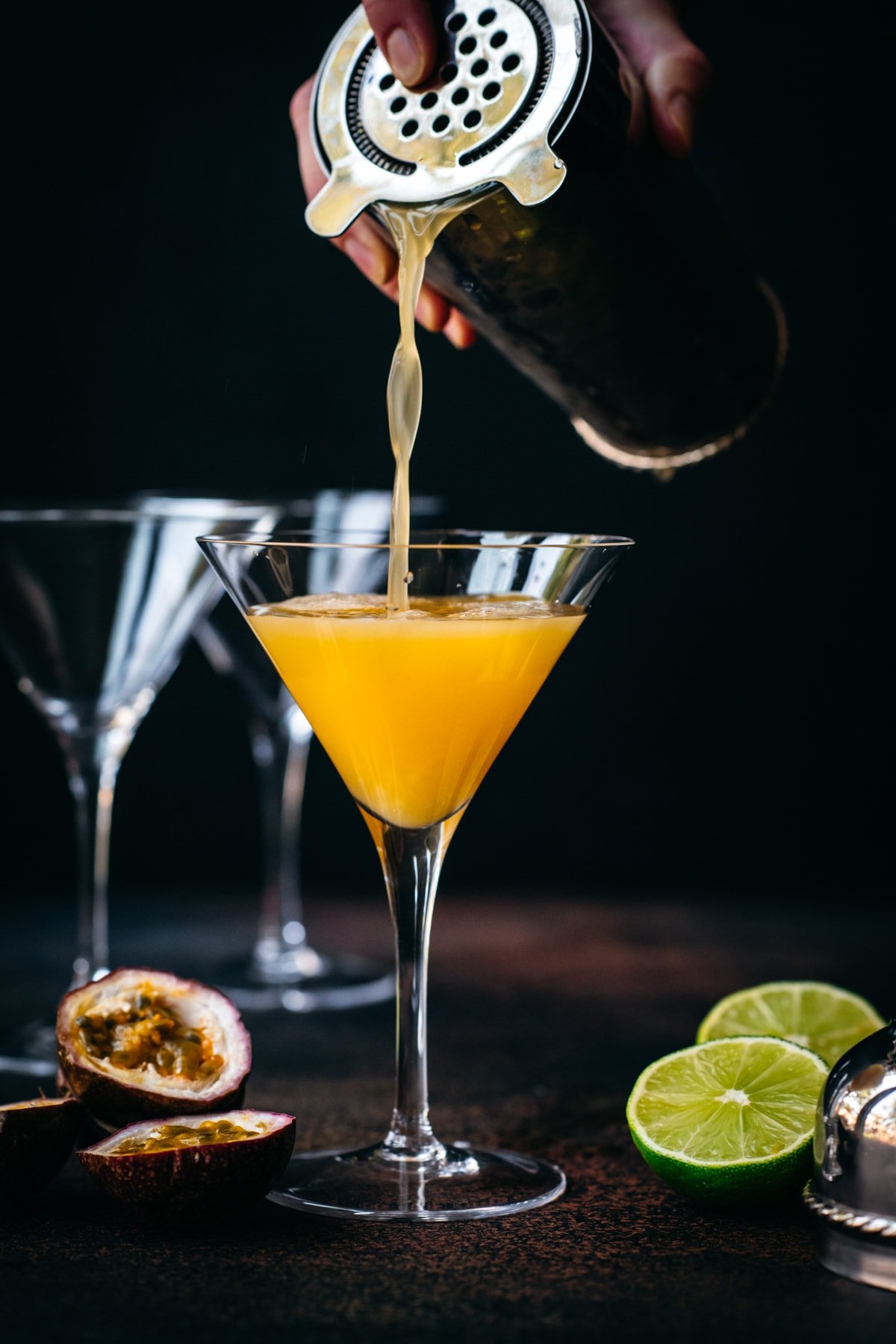 Pouring passion fruit martini into a glass from cocktail shaker.