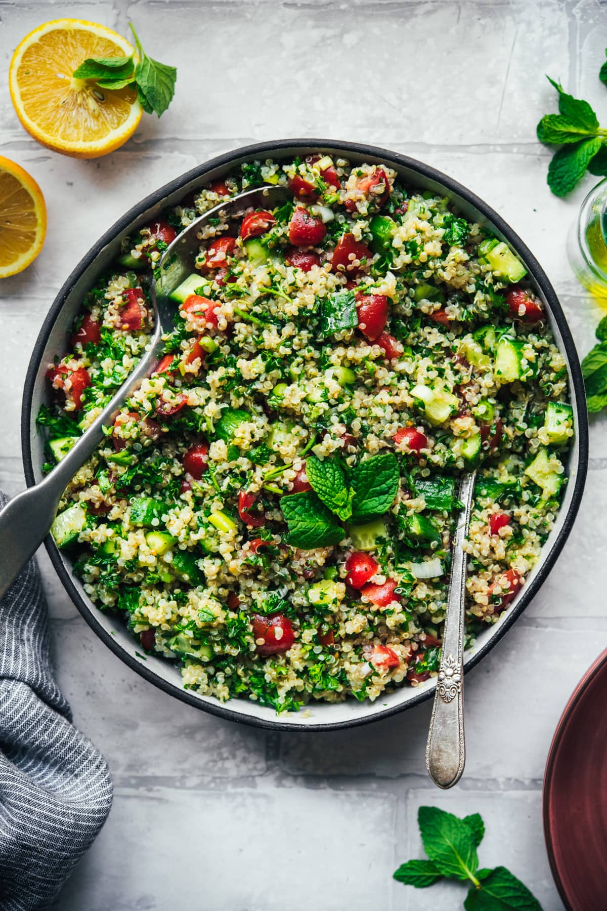 overhead view of vegan quinoa tabbouleh in a salad bowl with serving spoons. 