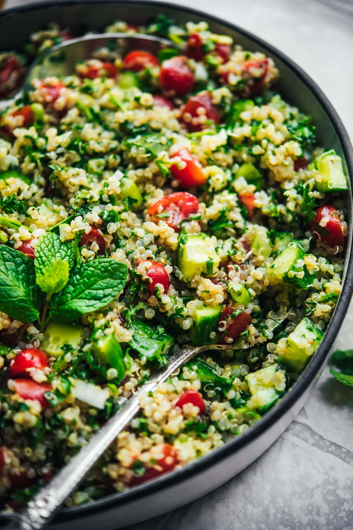 close up view of vegan quinoa tabbouleh in a salad bowl with serving spoons. 