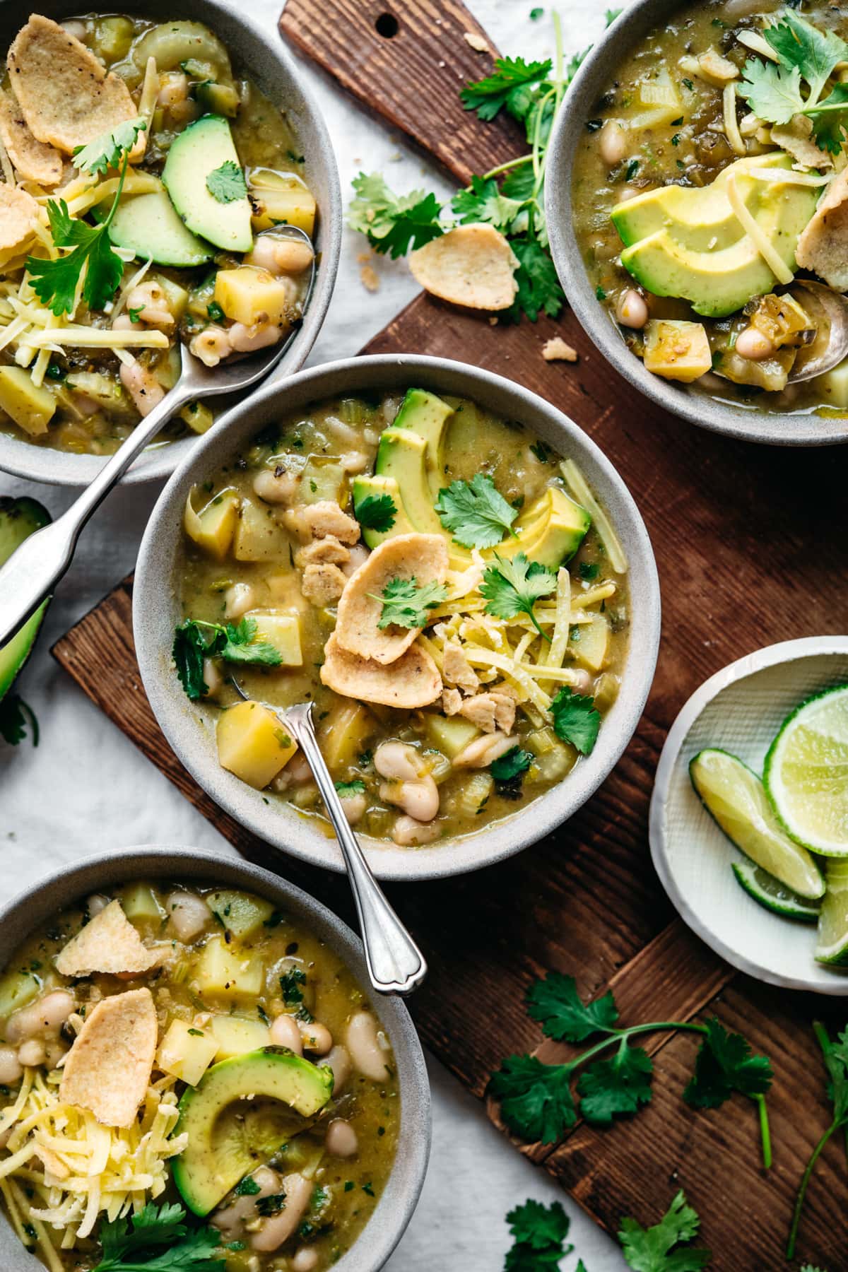 overhead view of bowls of vegan white bean chili topped with cheese, avocado and corn chips. 