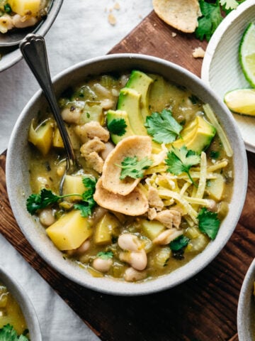 overhead view of bowl of vegan white bean chili topped with avocado and corn chips.