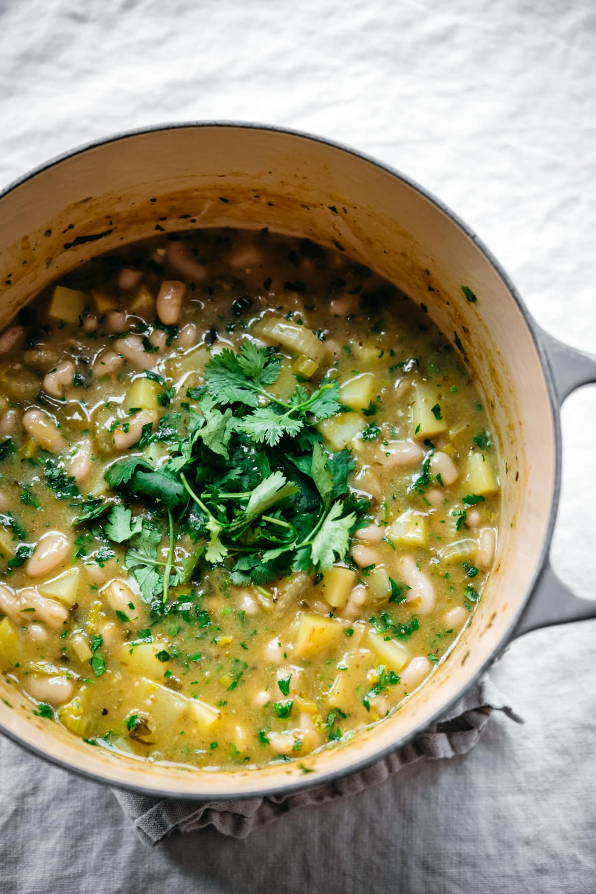 overhead view of vegan white bean chili in a large pot topped with fresh cilantro. 
