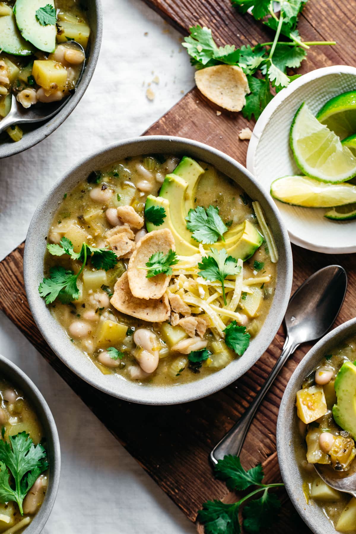 overhead view of bowls of vegan white bean chili topped with cheese, avocado and corn chips. 