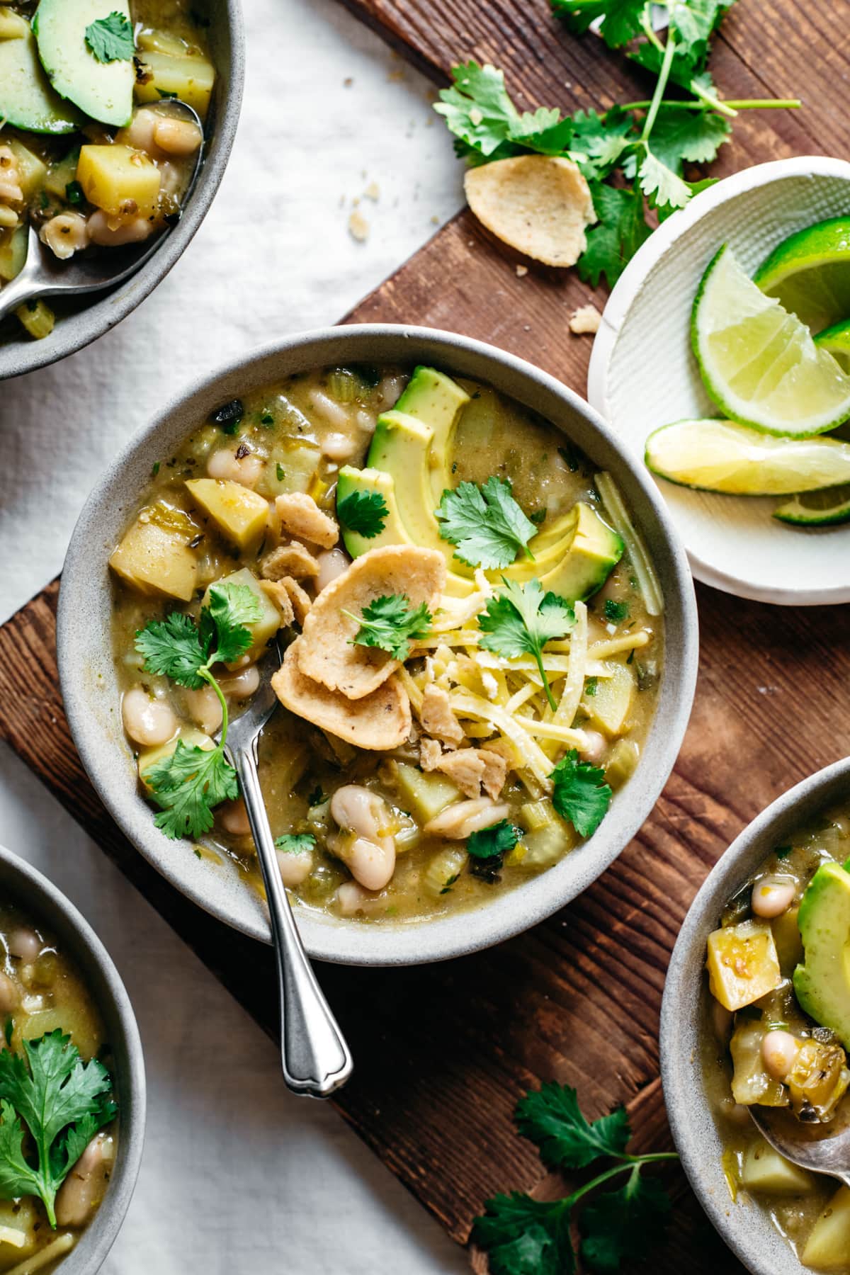 overhead view of bowls of vegan white bean chili topped with cheese, avocado and corn chips. 