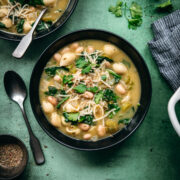 overhead view of white bean spinach soup topped with vegan parmesan in black soup bowl.