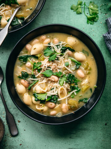 overhead view of white bean spinach soup topped with vegan parmesan in black soup bowl.