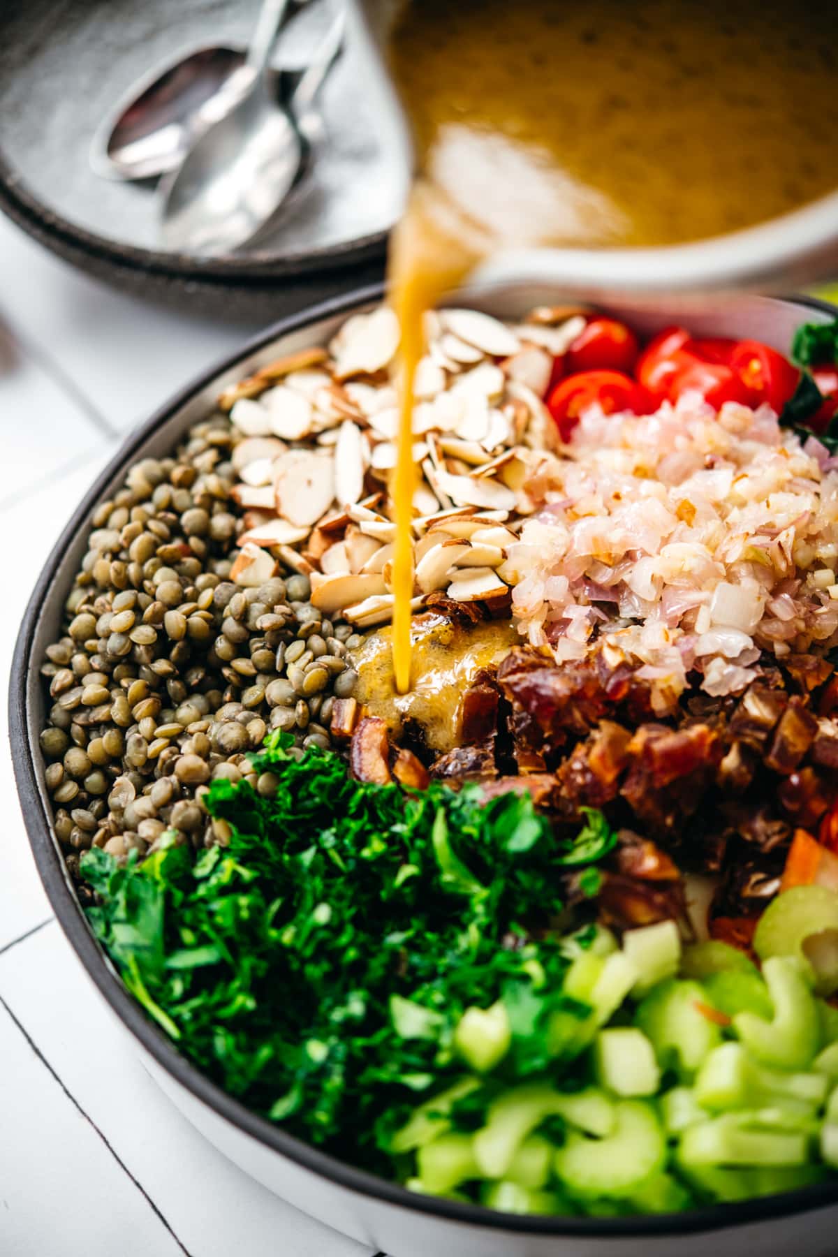 close up view of pouring vinaigrette onto french lentil and vegetable salad.