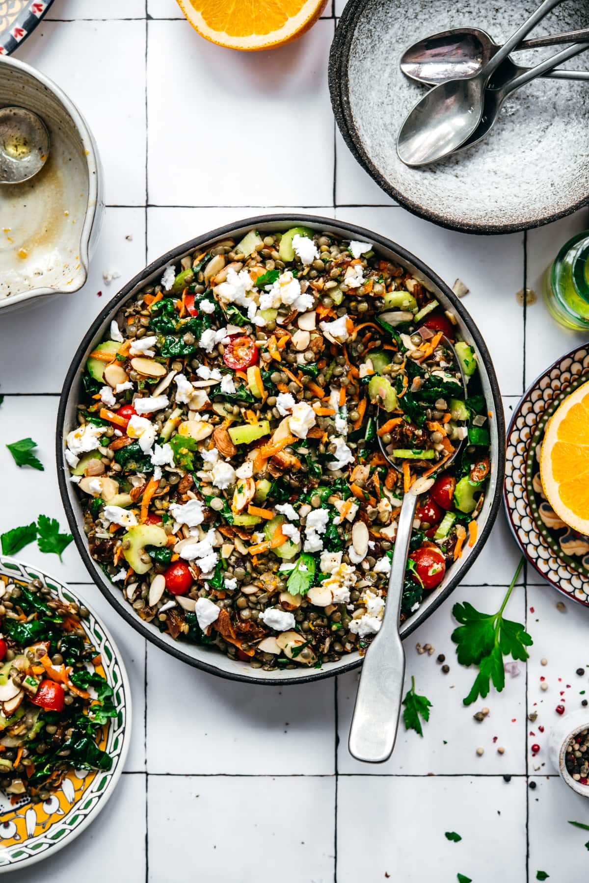 overhead view of vegan french lentil salad in a large bowl with serving spoon on white tile background.