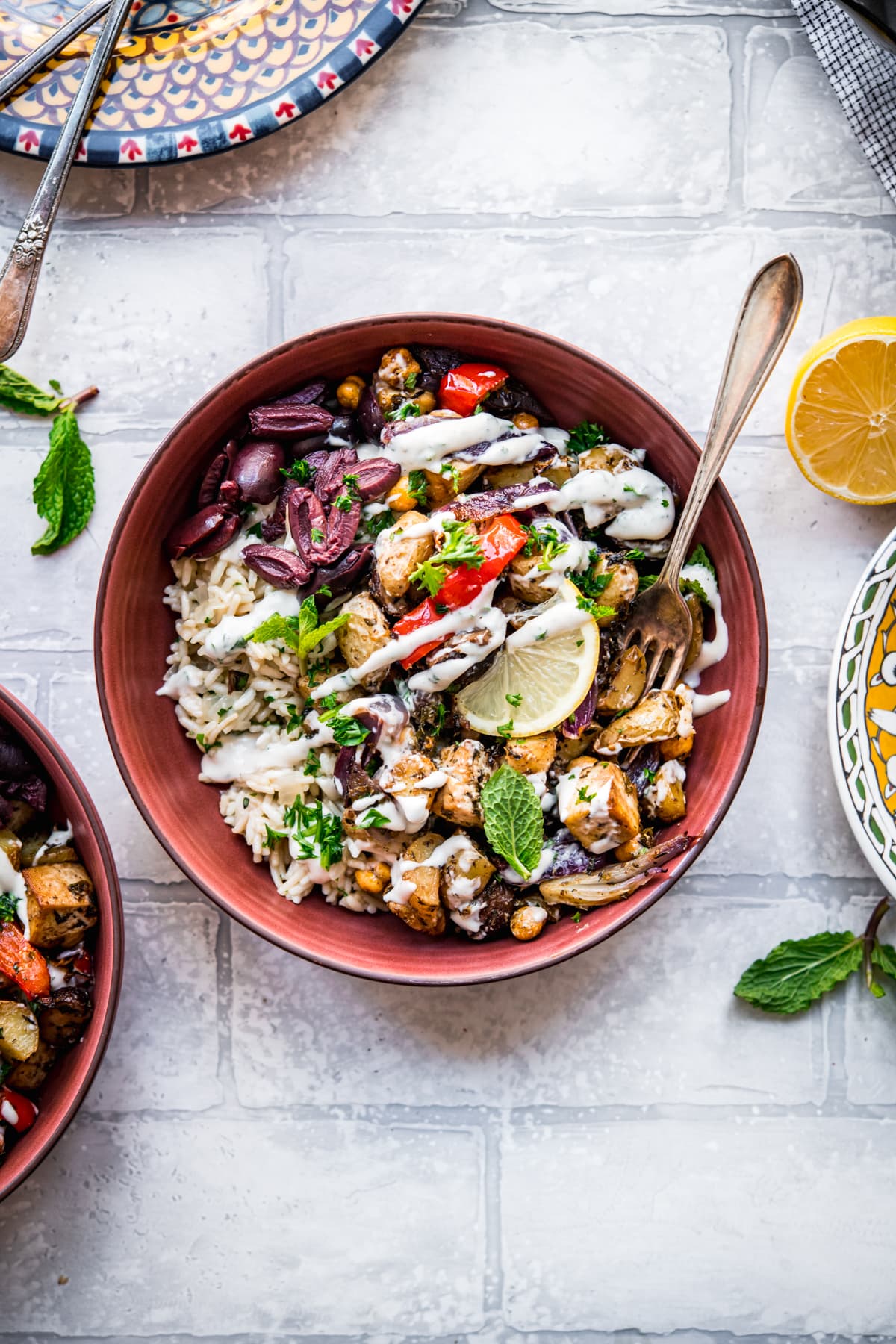 overhead view of Mediterranean roasted tofu and vegetables in a bowl over rice pilaf with yogurt tahini dressing.