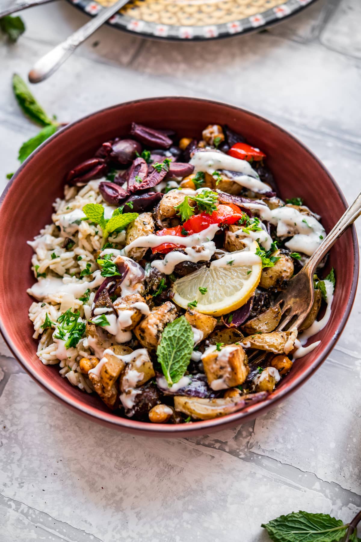 close up view of Mediterranean roasted tofu and vegetables in a bowl over rice pilaf with yogurt tahini dressing.