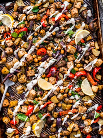 overhead view of vegan mediterranean sheet pan dinner with tofu, chickpeas, vegetables and tahini yogurt drizzle.