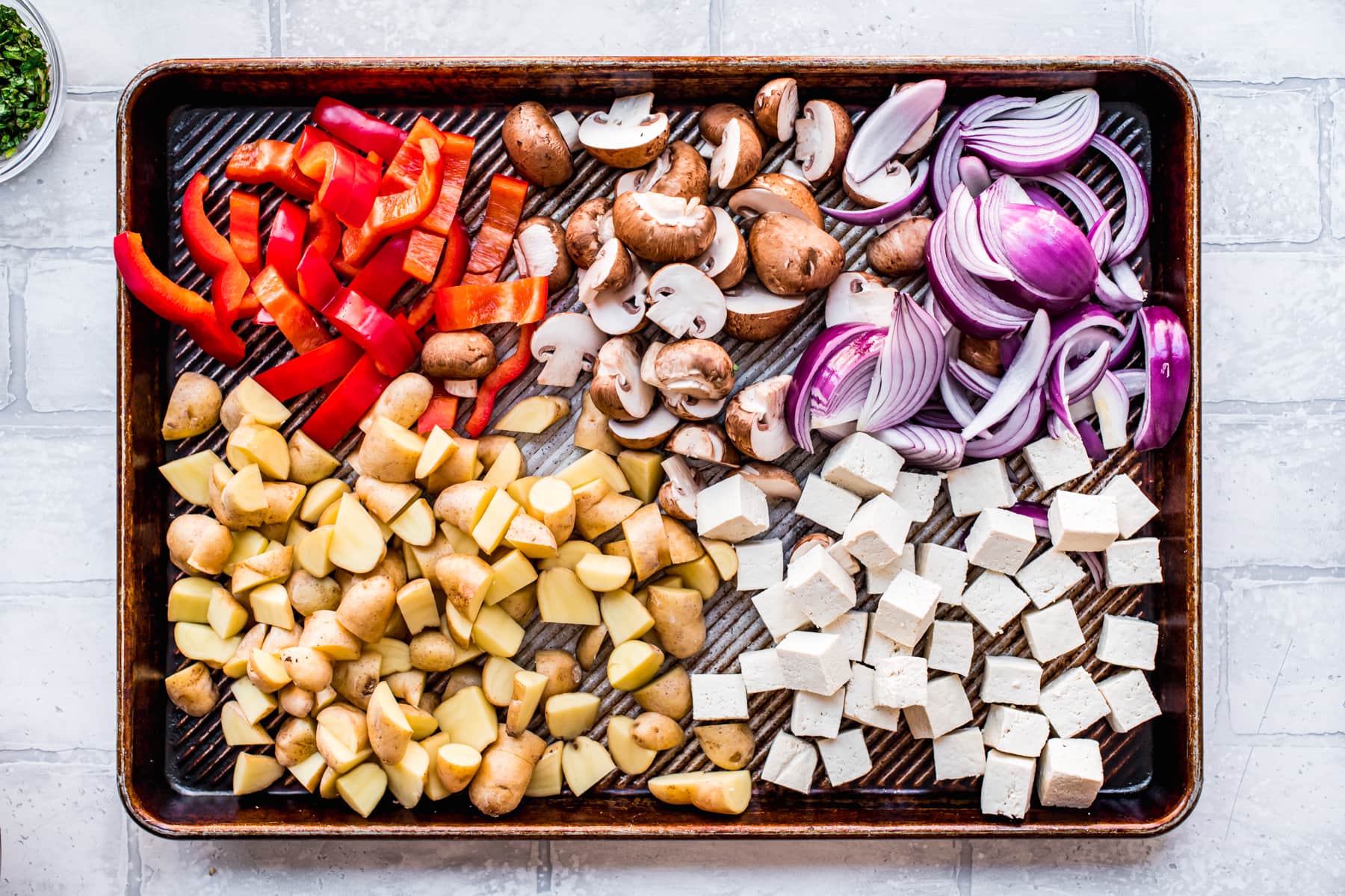 overhead view of vegan mediterranean sheet pan dinner with tofu and vegetables before roasting.