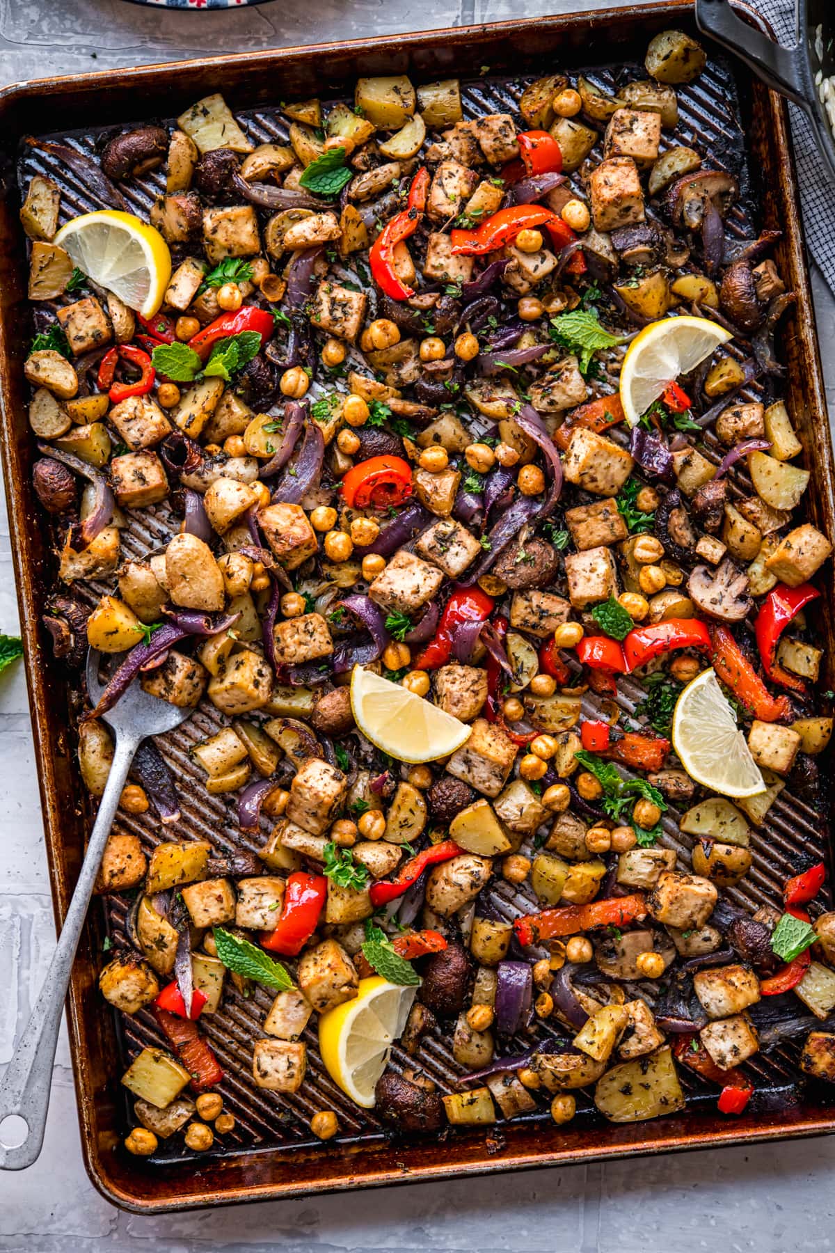 overhead view of vegan mediterranean sheet pan dinner with tofu, chickpeas and vegetables. 