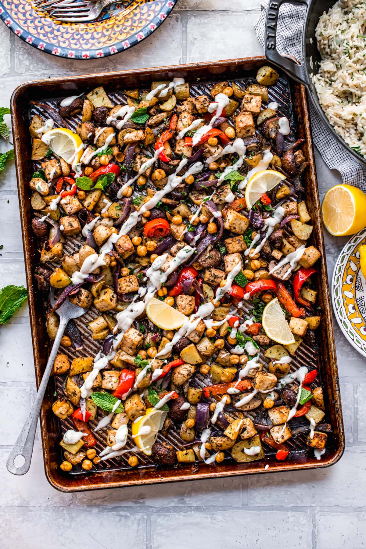 overhead view of vegan mediterranean sheet pan dinner with tofu, chickpeas, vegetables and tahini yogurt drizzle.