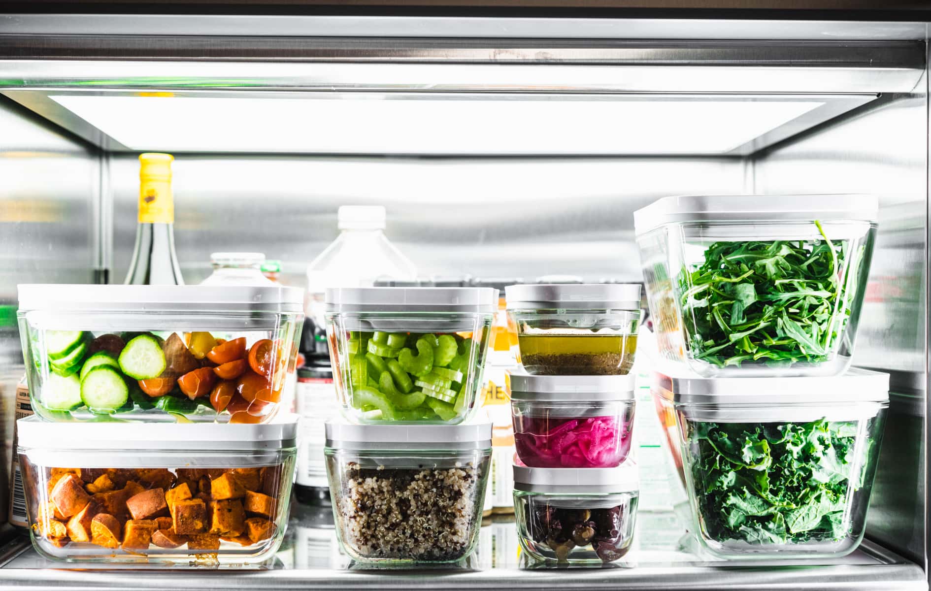 multiple meal prep containers stacked in a refrigerator filled with salad ingredients. 