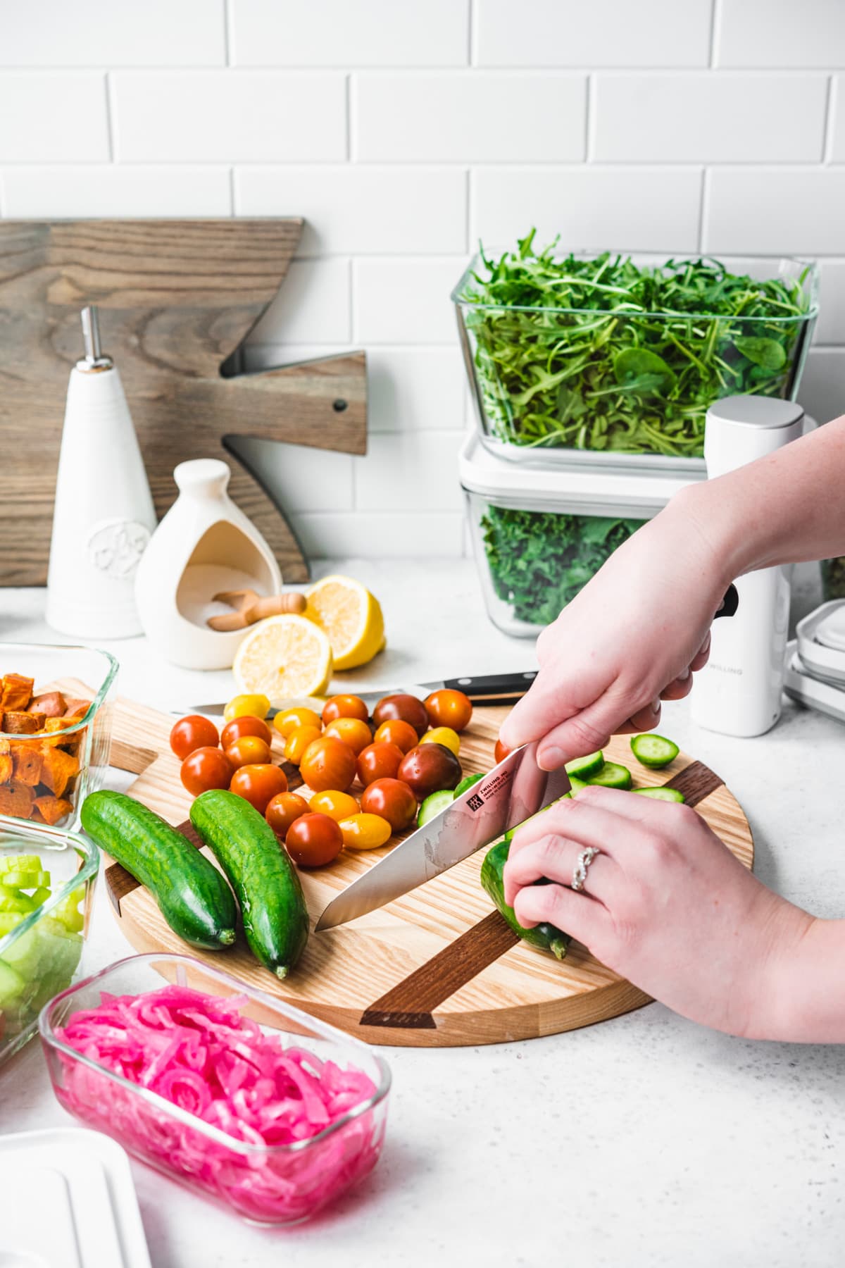 person slicing mini cucumbers and tomatoes on a wood cutting board.