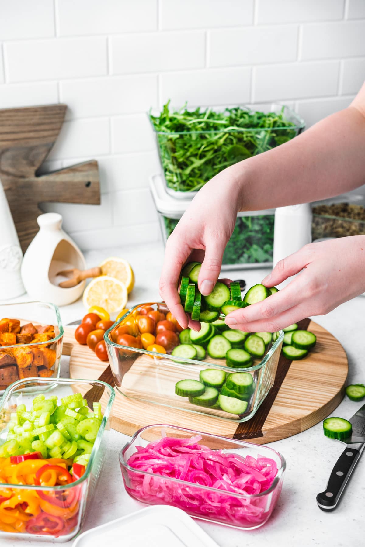 person putting sliced cucumbers into meal prep container. 