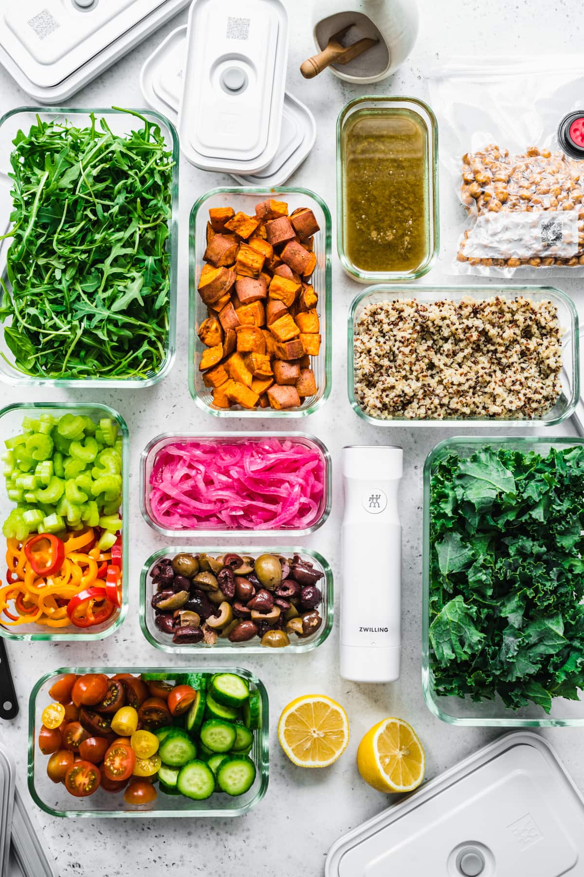 overhead view of several meal prep containers filled with various salad ingredients, like roasted and raw sliced vegetables, greens, quinoa, etc.