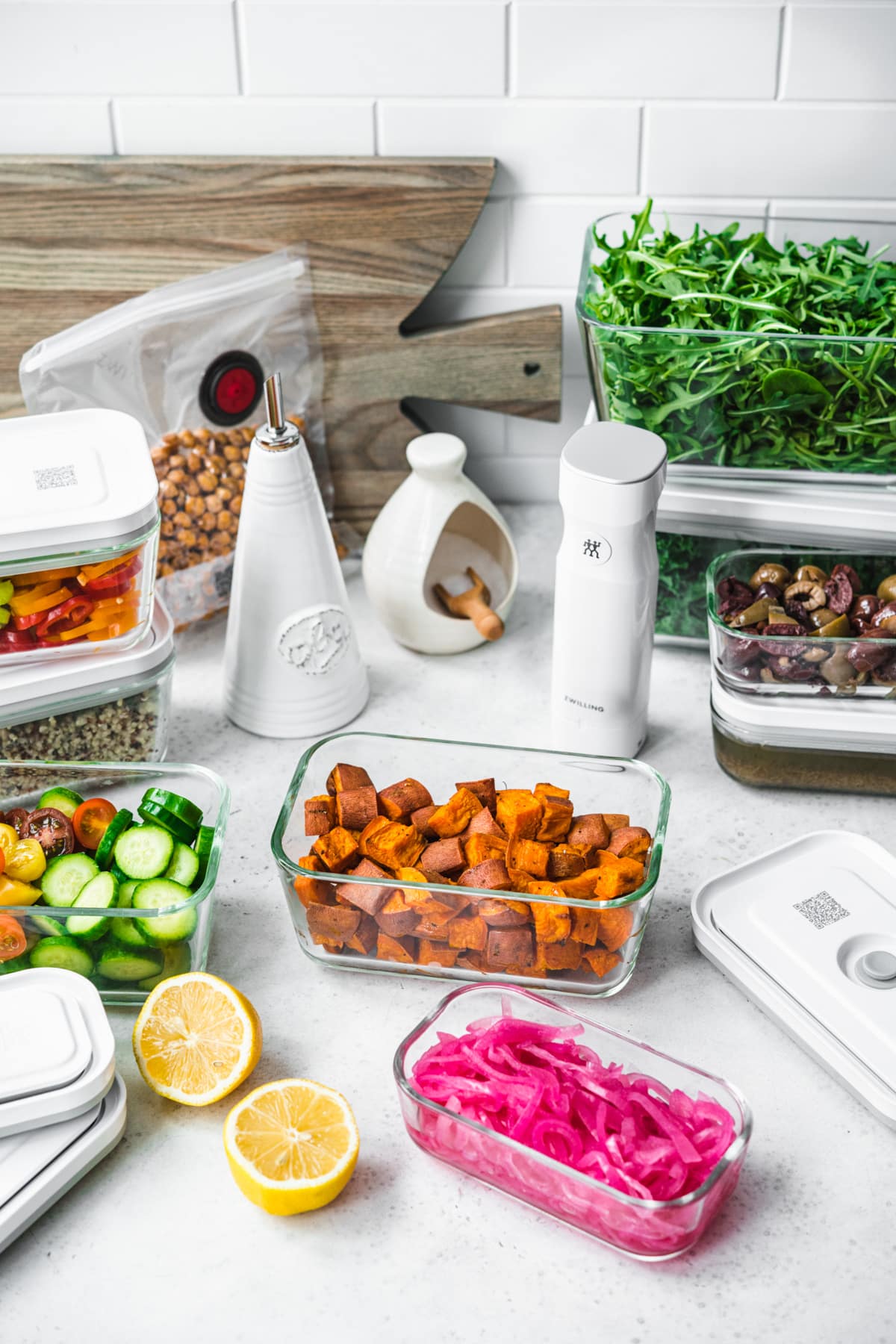 side view of several meal prep containers filled with salad ingredients, like greens, roasted sweet potato and fresh vegetables. 