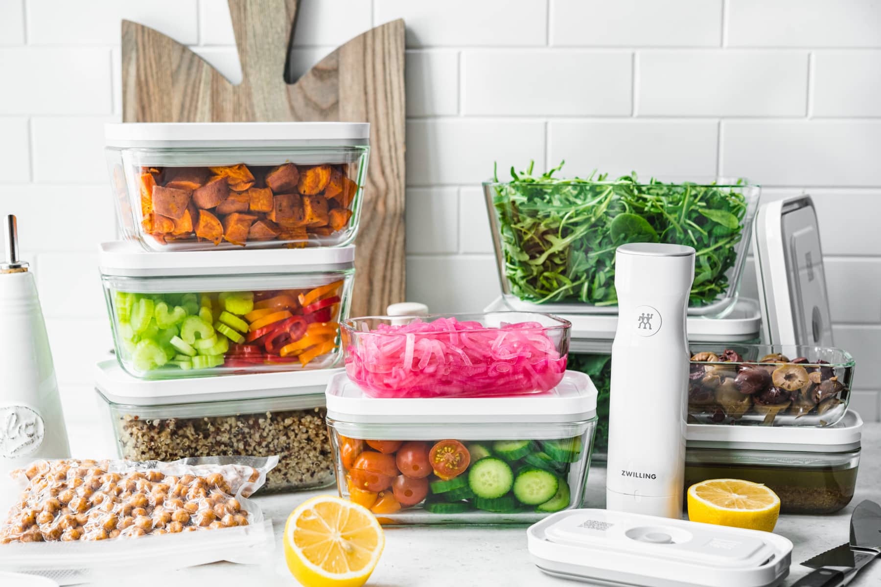 side view of several meal prep containers filled with salad ingredients, like greens, roasted sweet potato and fresh vegetables. 