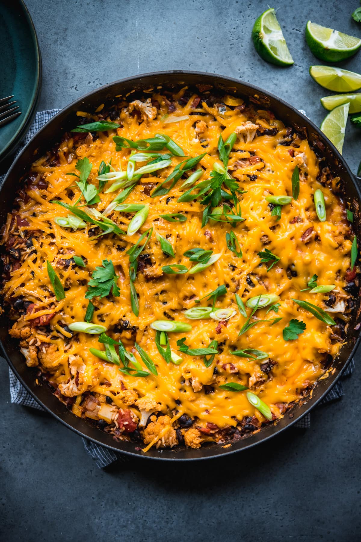 overhead view of vegan cheesy cauliflower bake with black beans and rice in large skillet. 