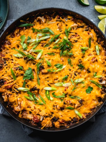 overhead view of vegan cheesy cauliflower bake with black beans and rice in large skillet.