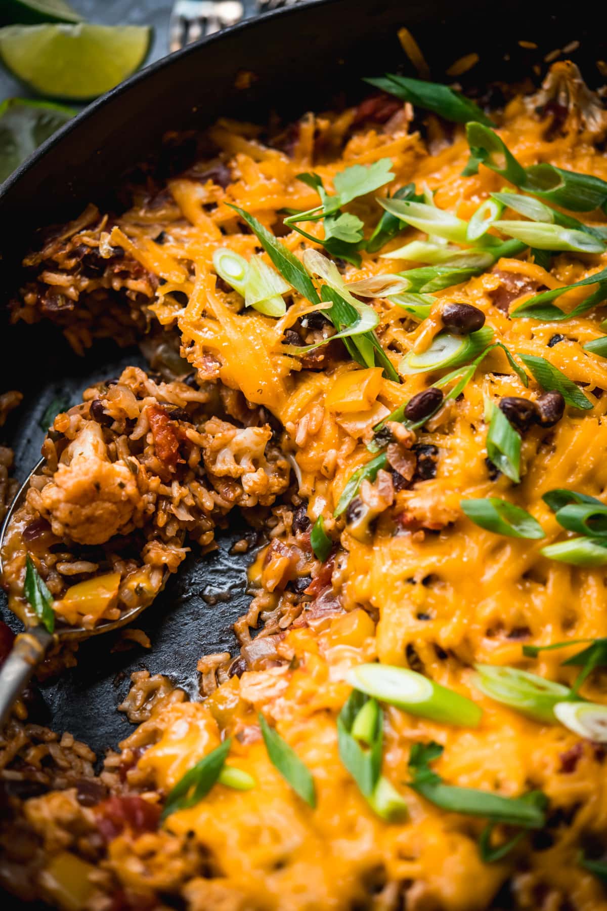 close up view of cheesy vegan cauliflower, rice and black bean bake in a skillet. 