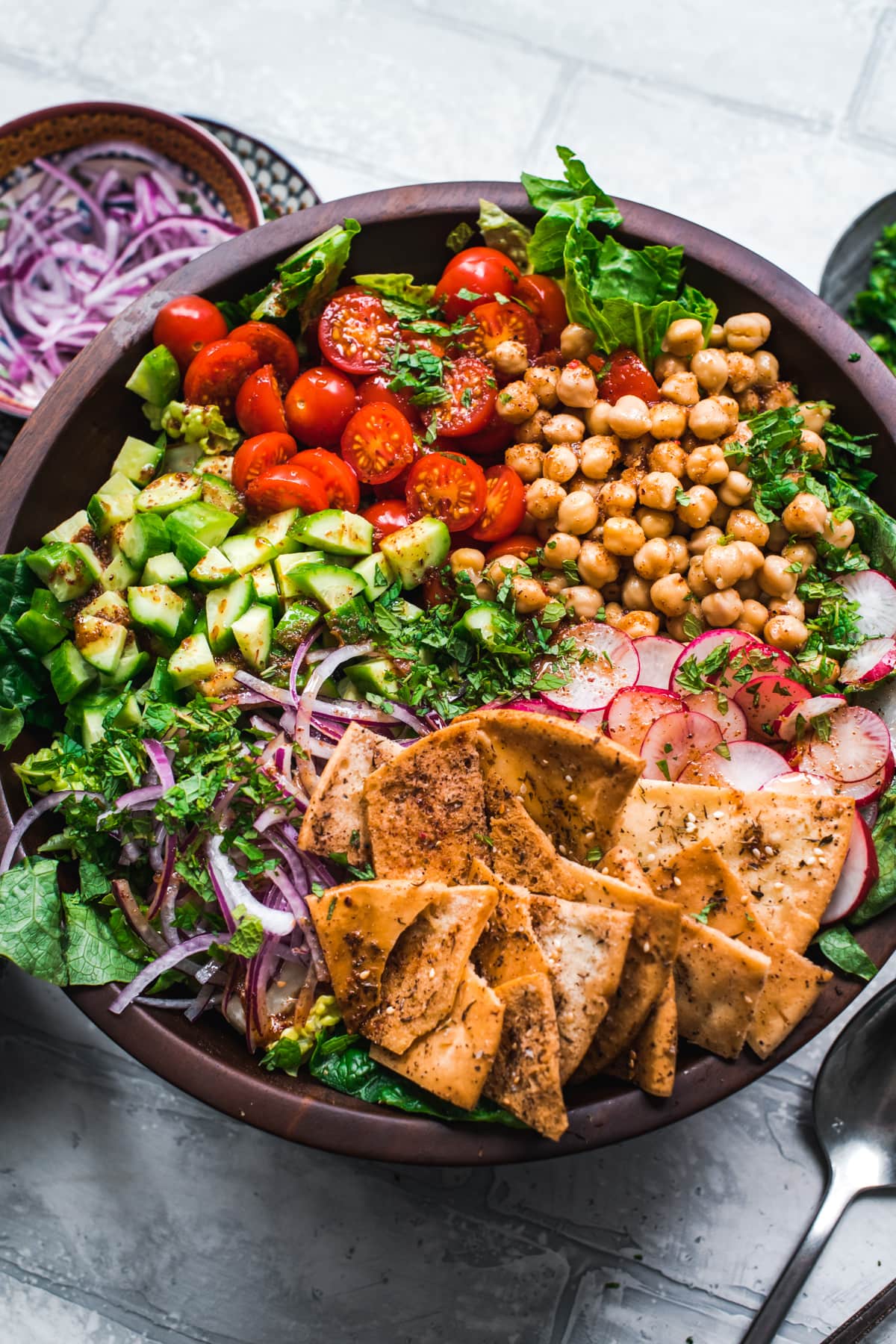 overhead view of chickpea fattoush salad with pita chips in wood salad bowl. 