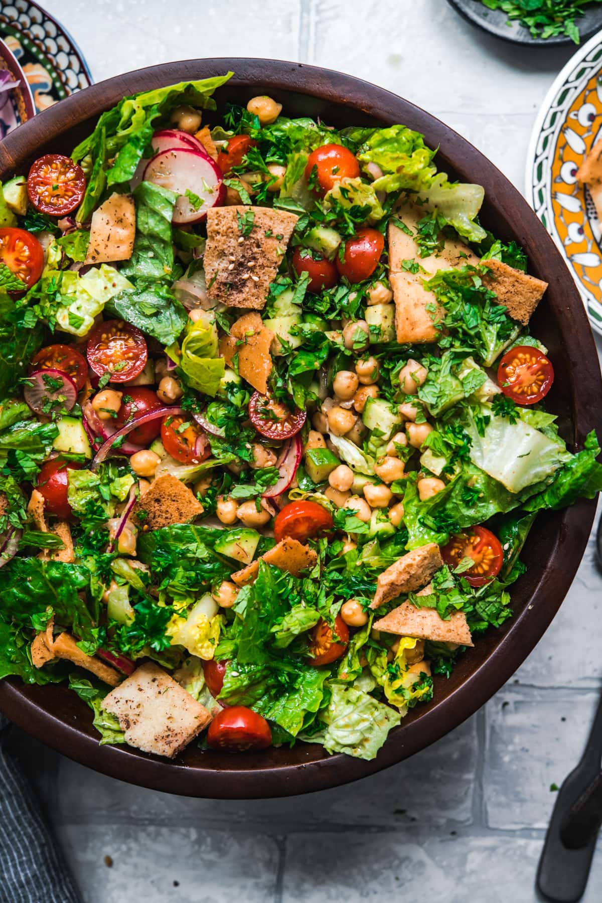 overhead view of chickpea fattoush salad with pita chips in wood salad bowl. 