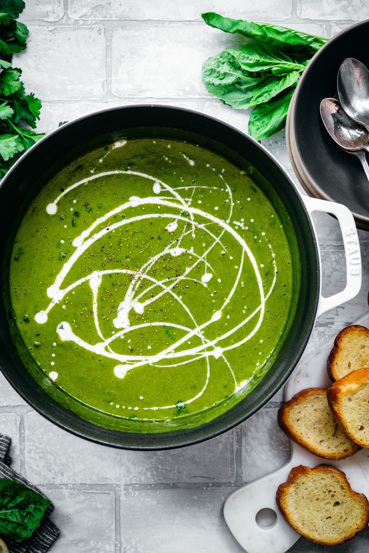 overhead view of creamy vegan kale potato soup with yogurt drizzle and fresh basil in a large white pot.