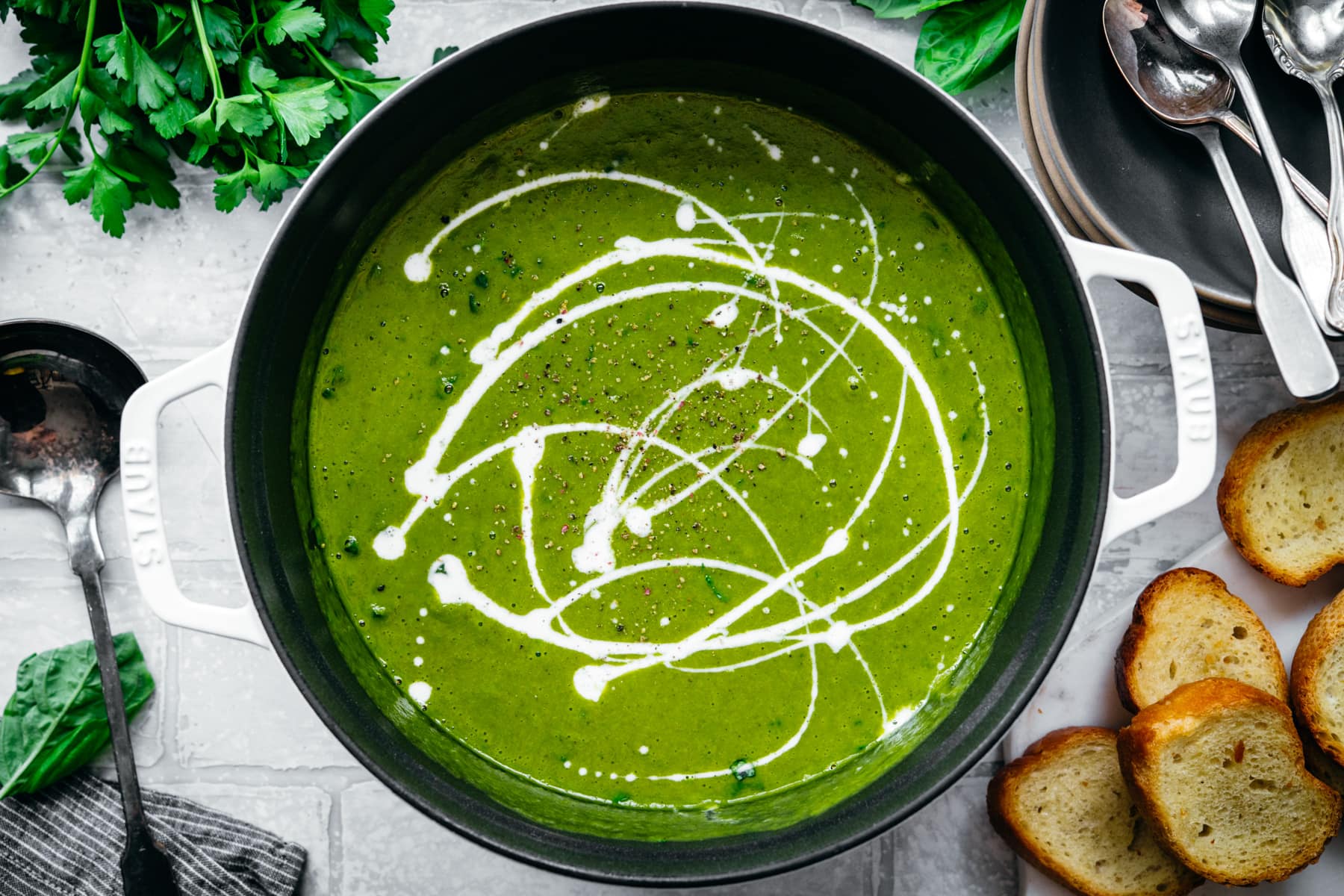 overhead view of creamy vegan kale potato soup with yogurt drizzle and fresh basil in a large white pot.