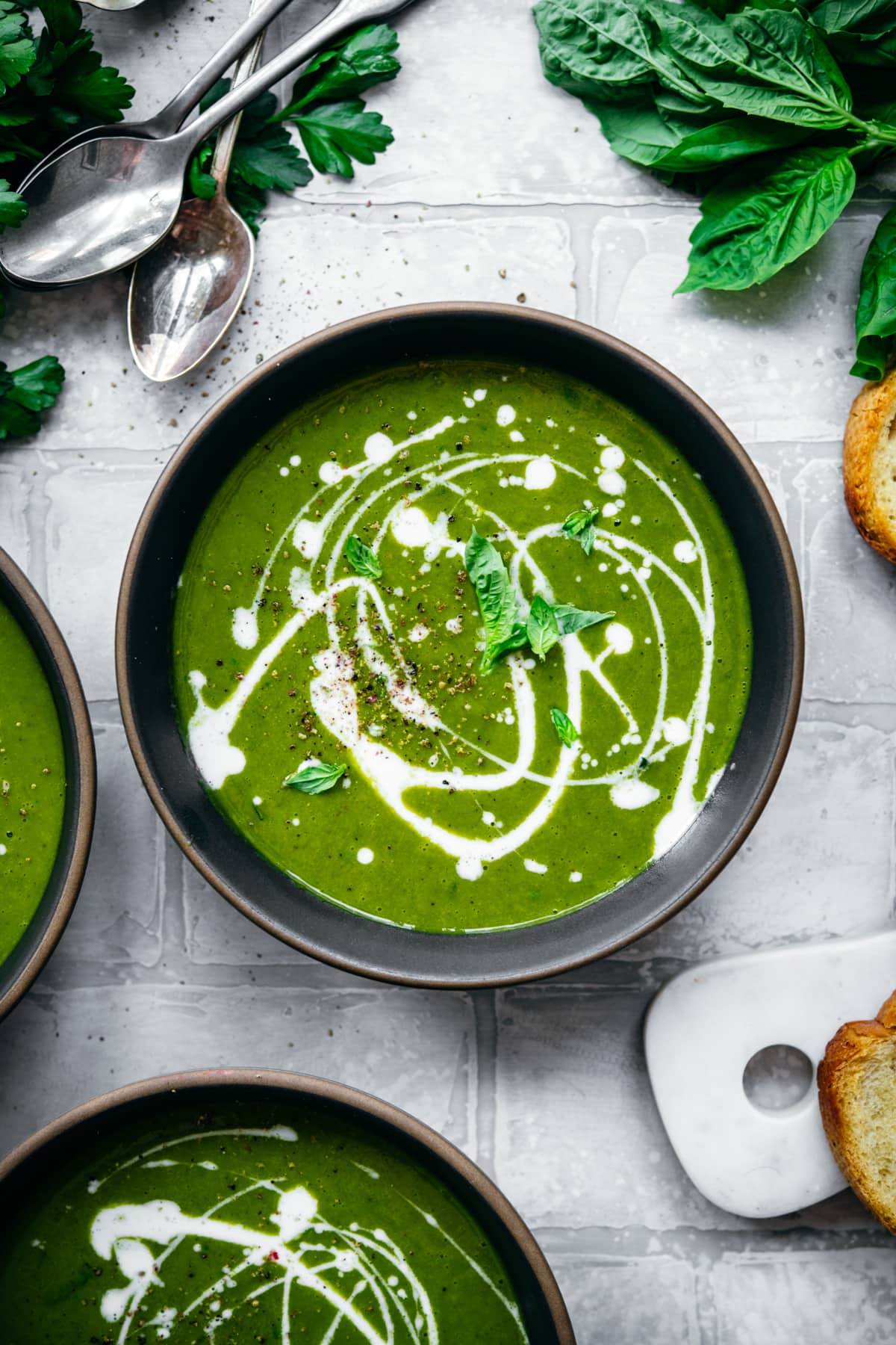 overhead view of vegan kale potato soup with yogurt drizzle and fresh basil. 