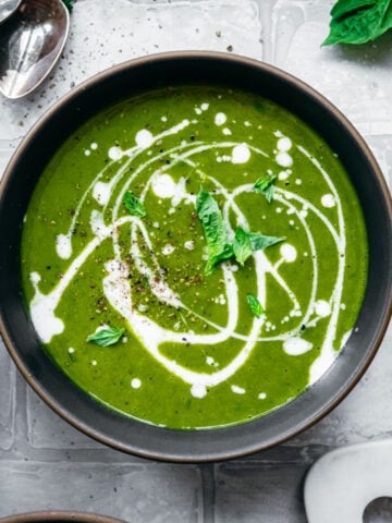 overhead view of vegan kale potato soup with yogurt drizzle and fresh basil.