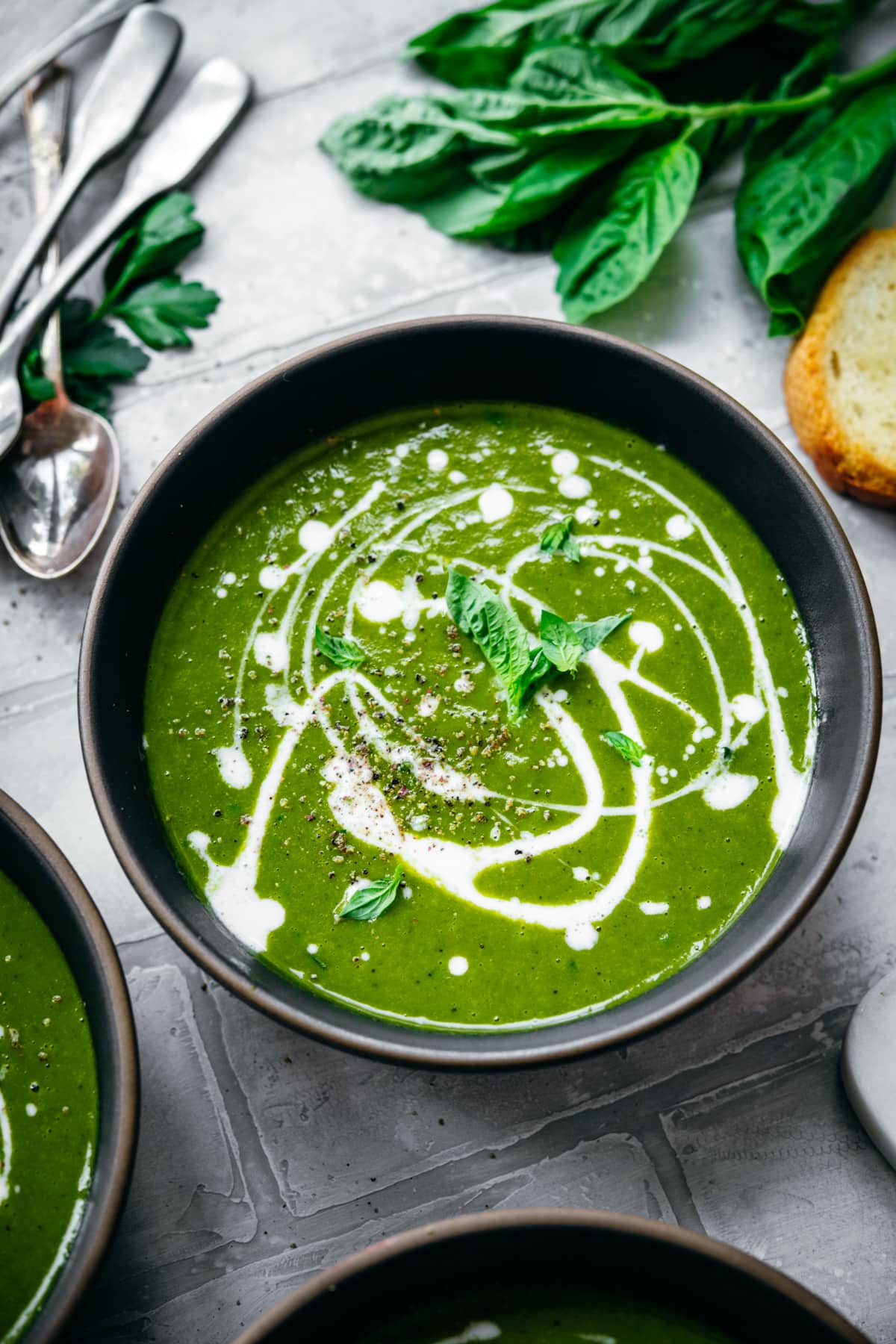 close up view of creamy potato kale soup in a bowl with yogurt drizzle and fresh basil.