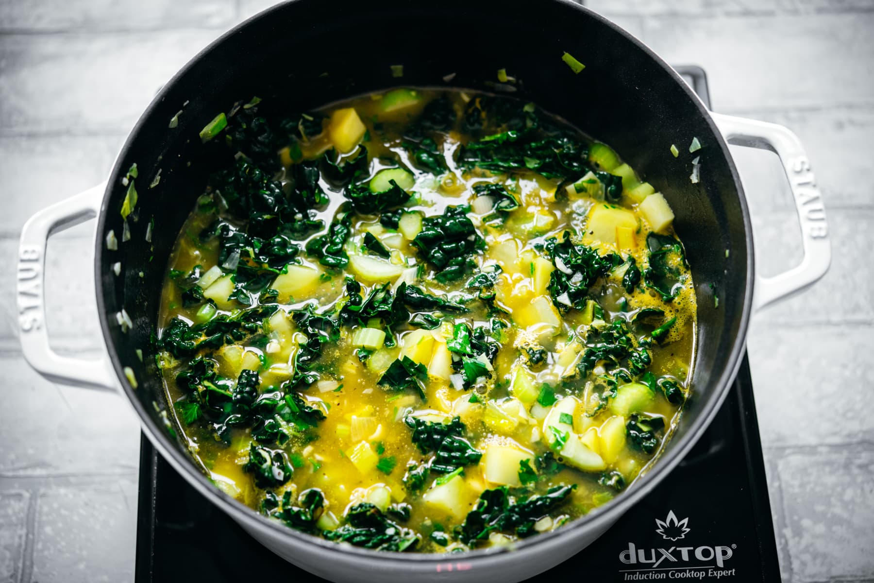 Potato kale soup in white pot.